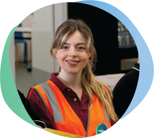 Smiling woman in Hi Vis Vest, sitting at a work bench
