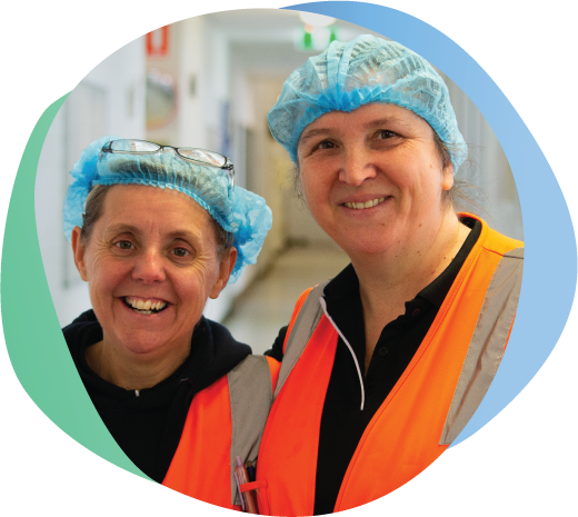 Two women smiling at camera, wearing hair nets and Hi Vis Vests.
