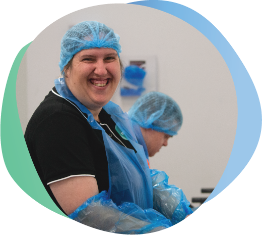 Person with disability wearing mobo shirt and hair net, apron and arm coverings working in sterile food room.